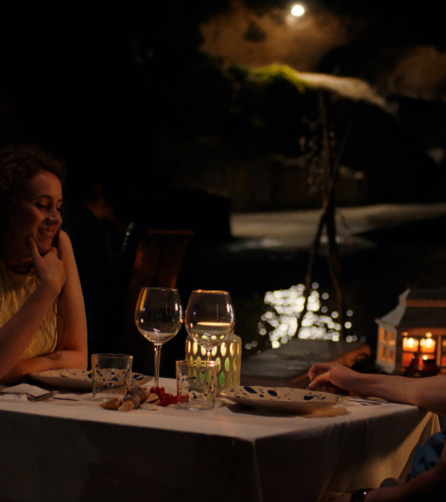 "Sense of Tumour - Freund von Devriendt": Tristan (Maarten Nulens) und Hanne (Marthe Schneider) sitzen sich am Tisch in einem Restaurant gegenüber und schauen sich aufrichtig an.