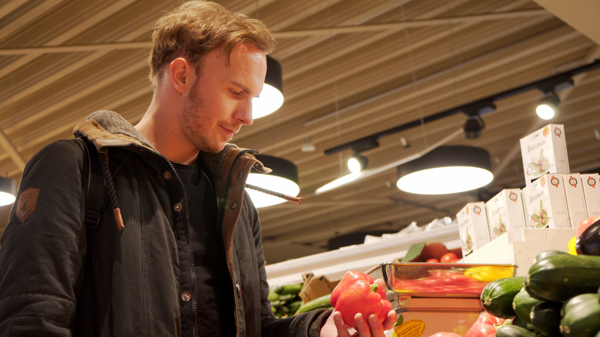 "plan b: Schluss mit Plastik -  Verpackung neu gedacht":  Christoph Schulz steht im Supermarkt vor losem Gemüse. Er hat eine Paprika in der Hand.
