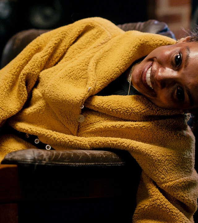 "Talk to Me": Mia (Sophia Wilde) sitzt auf einem Ledersessel und hat den Oberkörper zur Seite gedreht. Ihre Augen sind komplett schwarz, wodurch ihr Lächeln zu einer unheimlichen Grimasse wird.