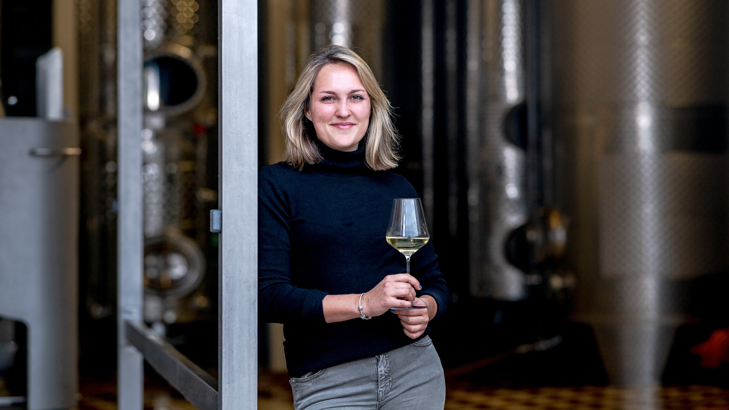 "37°Leben - In Papas Fußstapfen": Sophie Egert mit Weinglas vor der Kelterhalle des väterlichen Winzerbetriebs.