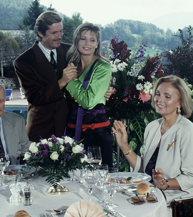 "Das Erbe der Guldenburgs - Die wahre Liebe": Margot (Ruth Maria Kubitschek) und Horst Strobel (Wolfgang Wahl) sitzen am Tisch und speisen. Jan (Sigmar Solbach) und Barbara (Sabine Postel) stehen eng umschlungen neben dem Tisch.