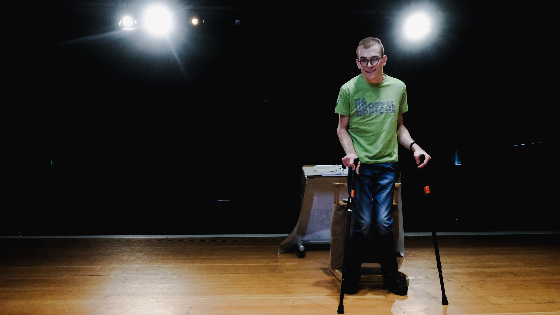 "einfach Mensch, Folge: Luis Adam: Lacht ruhig über mich!": Kabarettist Luis Adam steht unterstützt von zwei Krücken auf der Bühne.