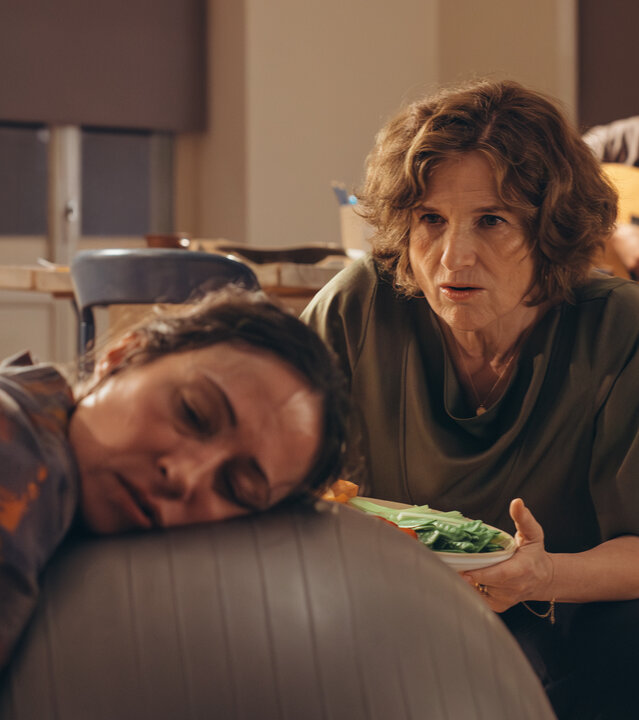 "PUSH - Trust the process": Raquel (Aenne Schwarz) liegt erschöpft mit ihrem Kopf auf einem Gymnastikball. Marcela (Victoria Trauttmansdorff) kniet neben ihr mit einem Gemüseteller und spricht mit Raquel. Leandro (James Newton) sitzt dahinter und spielt Gitarre. Greta (Lydia Amasko) sitzt im Hintergrund.