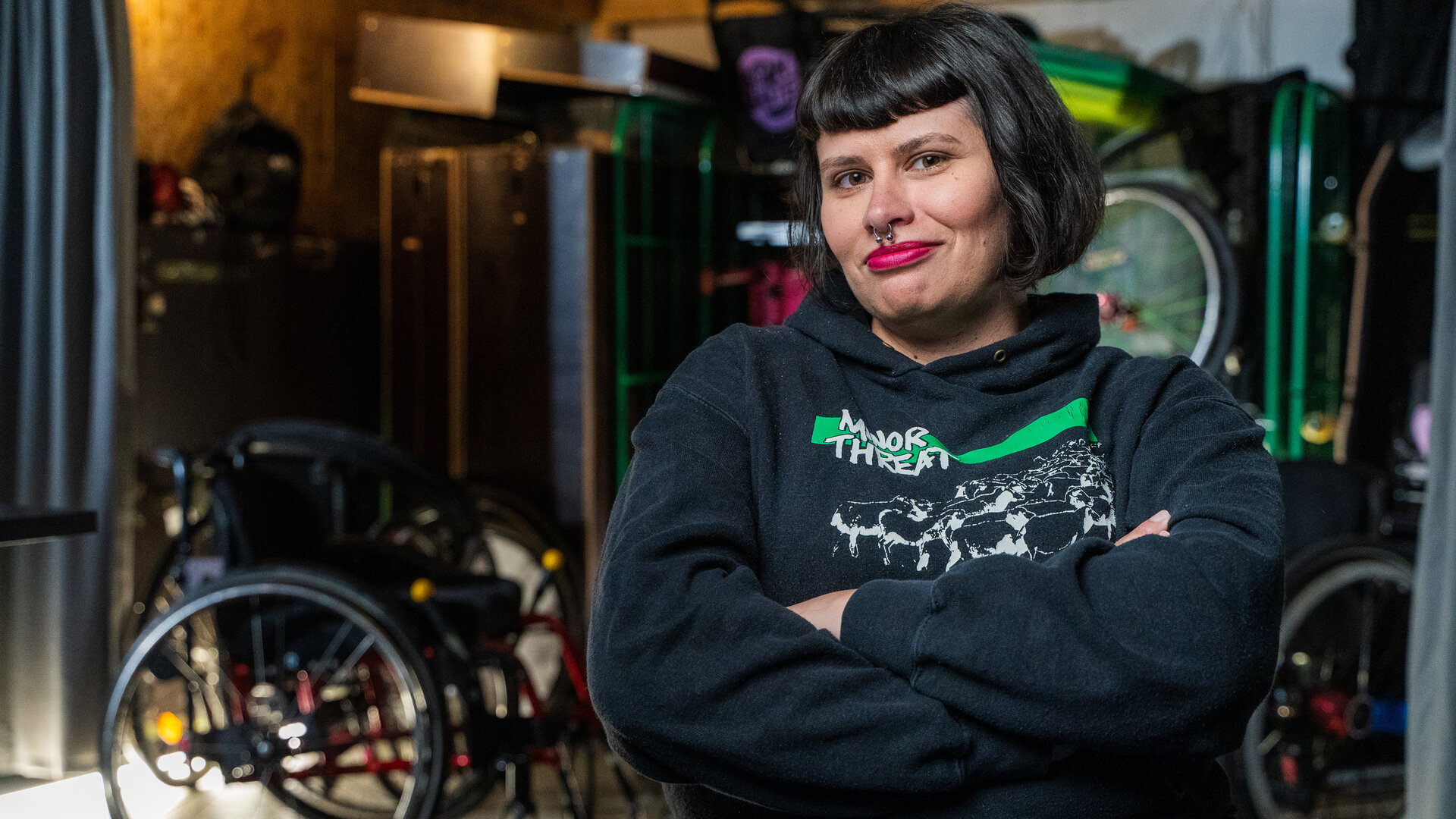 "einfach Mensch - Lisa Lebuser: Im Rollstuhl Grenzen sprengen": Die Protagonistin Lisa Lebuser sitzt in einem Raum und schaut lächelnd in die Kamera. Im Hintergrund stehen mehrere Rollstühle.