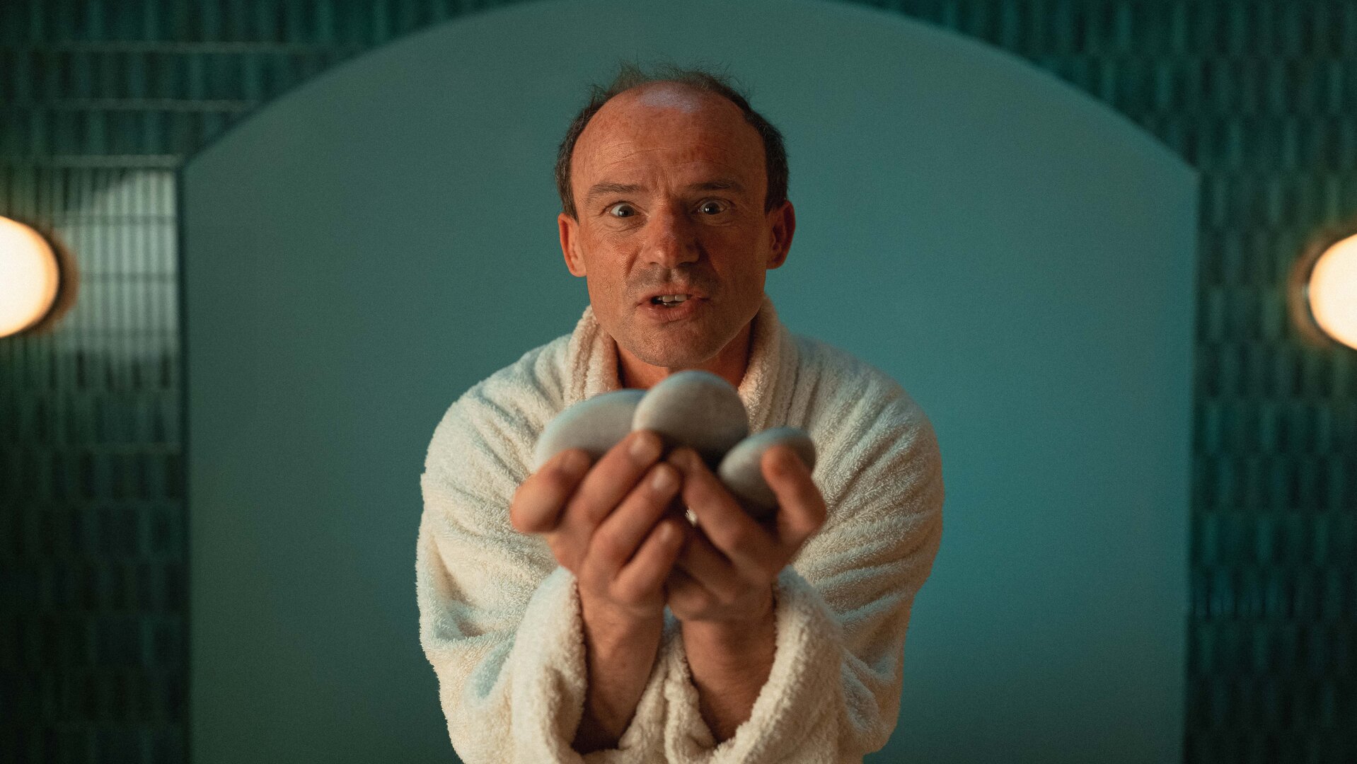 "Schlechte Menschen - Der Nörgler": Gustav (Gerhard Liebmann) hält drei flache Steine anbietend vor sich und sieht intensiv in die Kamera.