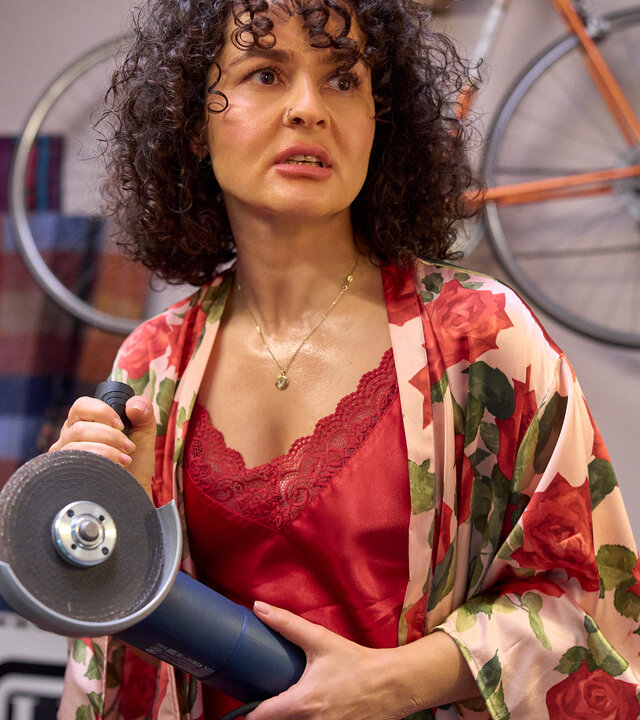 "Ich dich auch! - Der Stichtag": Jackie (Nagmeh Alaei) steht im Spitzennachthemd völlig aufgelöst im Raum. Sie hält eine Schneidemaschine in den Händen.