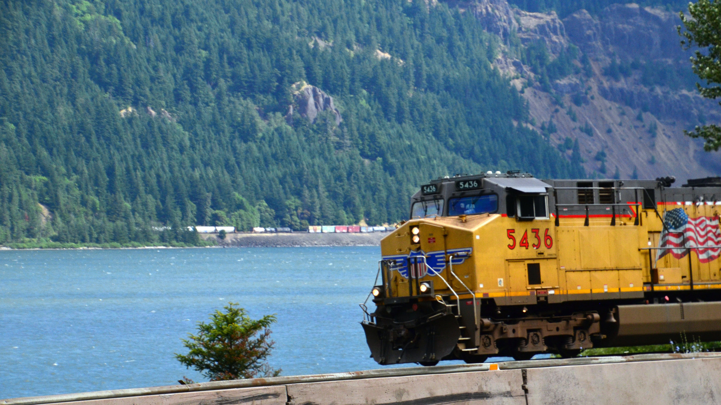"Bahnknoten Portland": Am Fluss ist viel Betrieb. Ganz klein im Hintergrund ist ein weiterer Güterzug zu sehen, der sich am anderen Flussufer Richtung Portland bewegt.