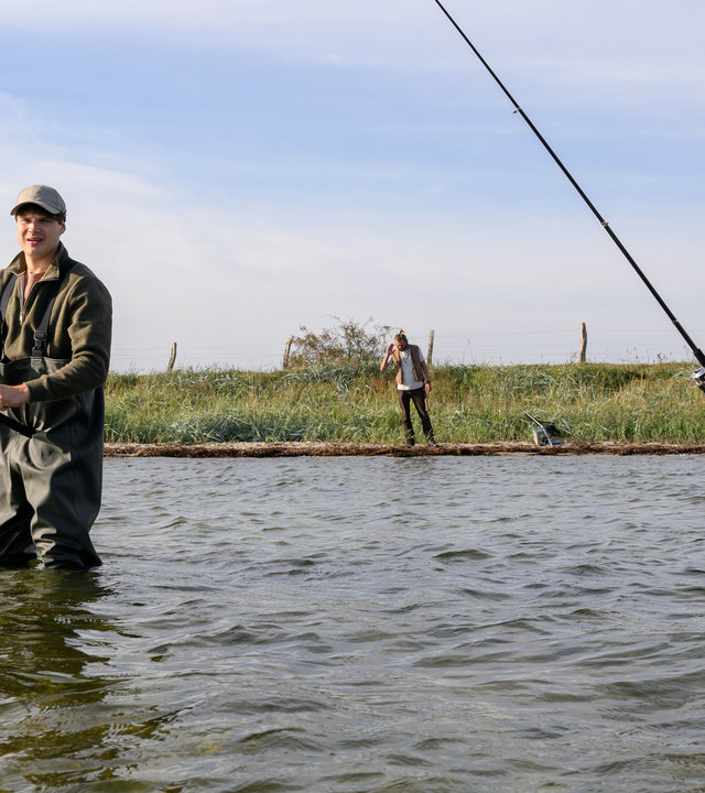"SOKO Wismar - Grabräuber": Jan-Hinrich Reuter (Udo Kroschwald) und Eddi Jansons (Gustavs Gailus) stehen im Wasser und angeln. Am Ufer steht Gunnar Schmied (Zhenja Isaak).