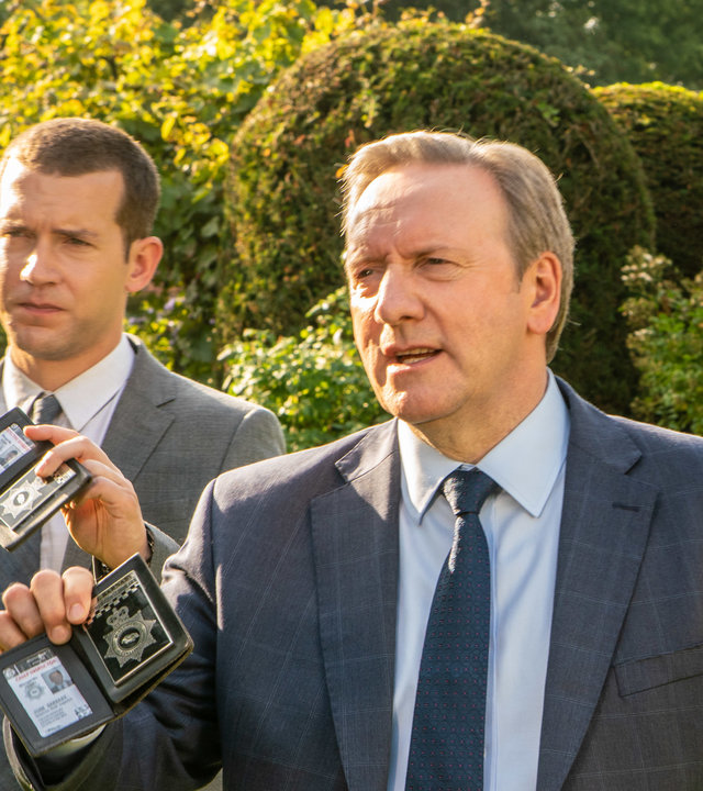 "Inspector Barnaby - Der Stachel des Todes": DCI John Barnaby (Neil Dudgeon) und DS Jamie Winter (Nick Hendrix) gehen nebeneinander über einen gepflegten Rasen. Sie halten ihrer Dienstmarken hoch, um sich als Polizisten zu erkennen zu geben.