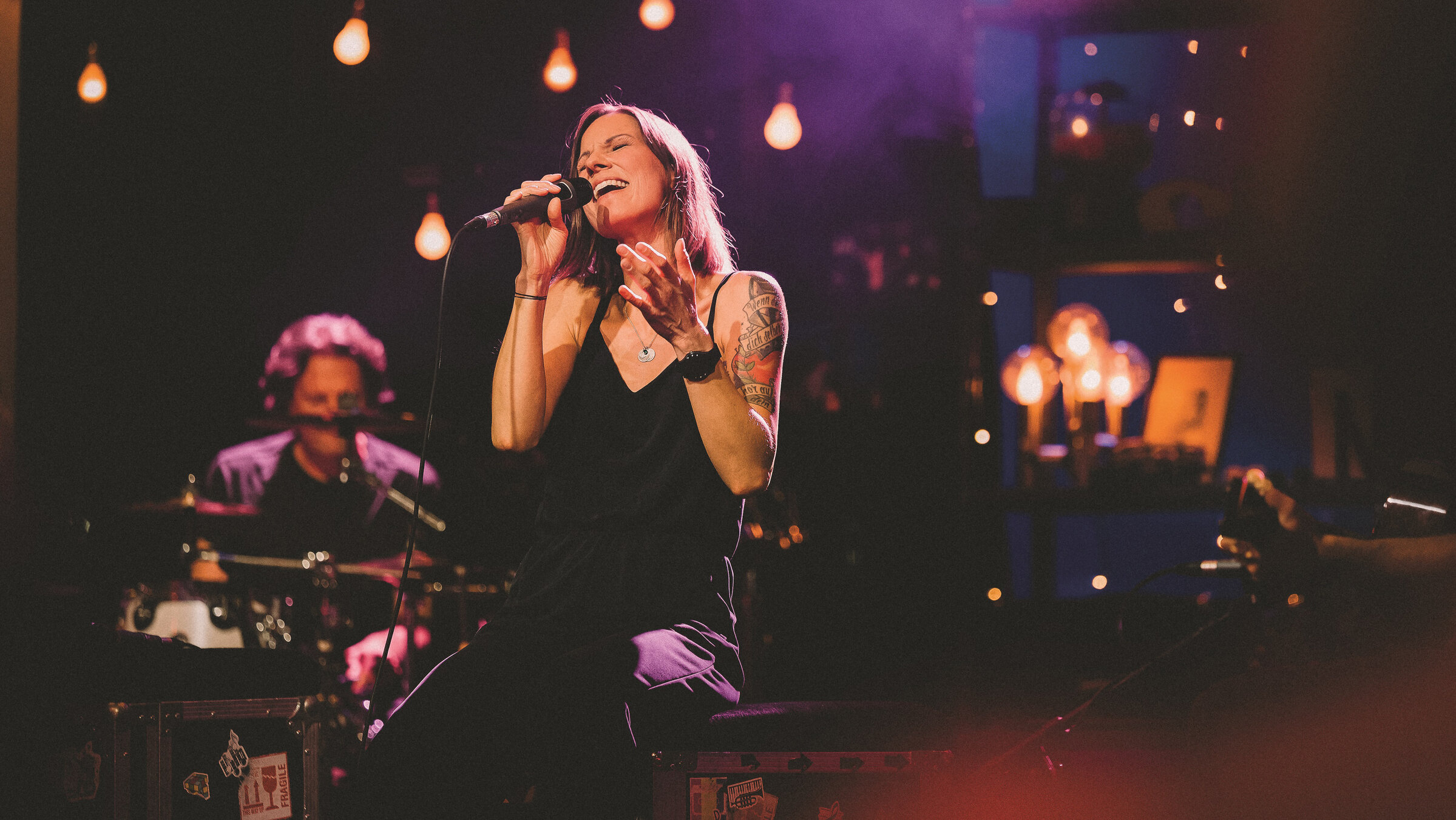 "Christina Stürmer: MTV Unplugged in Wien": Die Sängerin Christina Stürmer während eines Konzerts. Sie sitzt auf einem Schemel, ein Bein angewinkelt. Sie singt in ein Mikrofon. Die Augen sind geschlossen. Eine Hand zeigt nach vorne. Gekleidet ist sie mit einer schwarzen Hose und einem schwarzen Top.