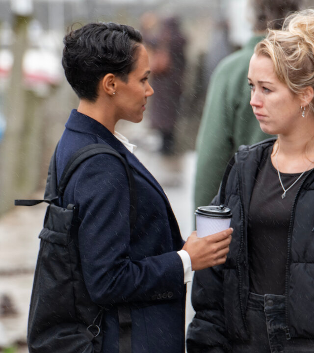 "Beyond Paradise - Der Ring": Hayley Collins (Hannah Traylen) und Kate Nolan (Lily Frazer) stehen sich auf der Straße gegenüber und schauen sich an. Beide halten Kaffeebecher in der Hand.