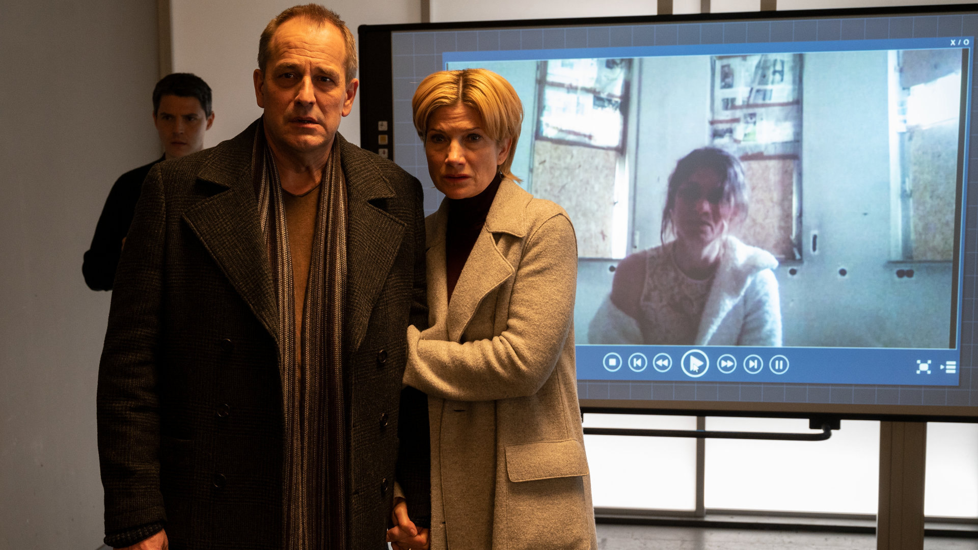 "SOKO Stuttgart – Doppeltes Spiel (2)": Die Lage ist ernst – das ist in den Gesichtern der ersten Kriminalhauptkommissarin Martina Seiffert (Astrid M. Fünderich), ihrem Mann Richard (Stephan Schad) und Kriminalkommissar Rico Sander (Benjamin Strecker) zu erkennen. Sie stehen im Konferenzraum, Martina hält ihren Mann am Arm und im Hintergrund ist ein Video der verweinten Cordula (Anna Bullard) zu sehen.