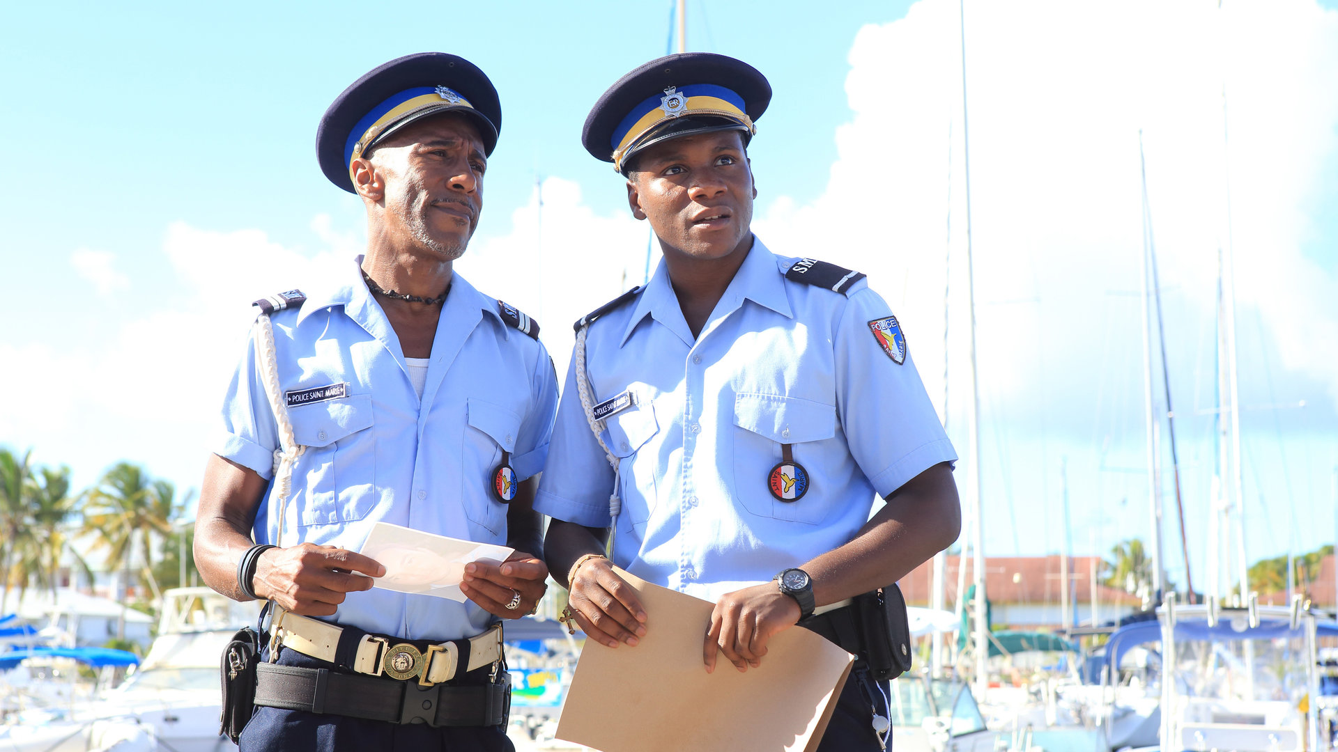 "Death in Paradise - Eiskalter Mord": Dwayne Myers (Danny John-Jules) und JP (Tobi Bakare) stehen nebeneinander in einem Jachthafen und blicken in die Ferne.