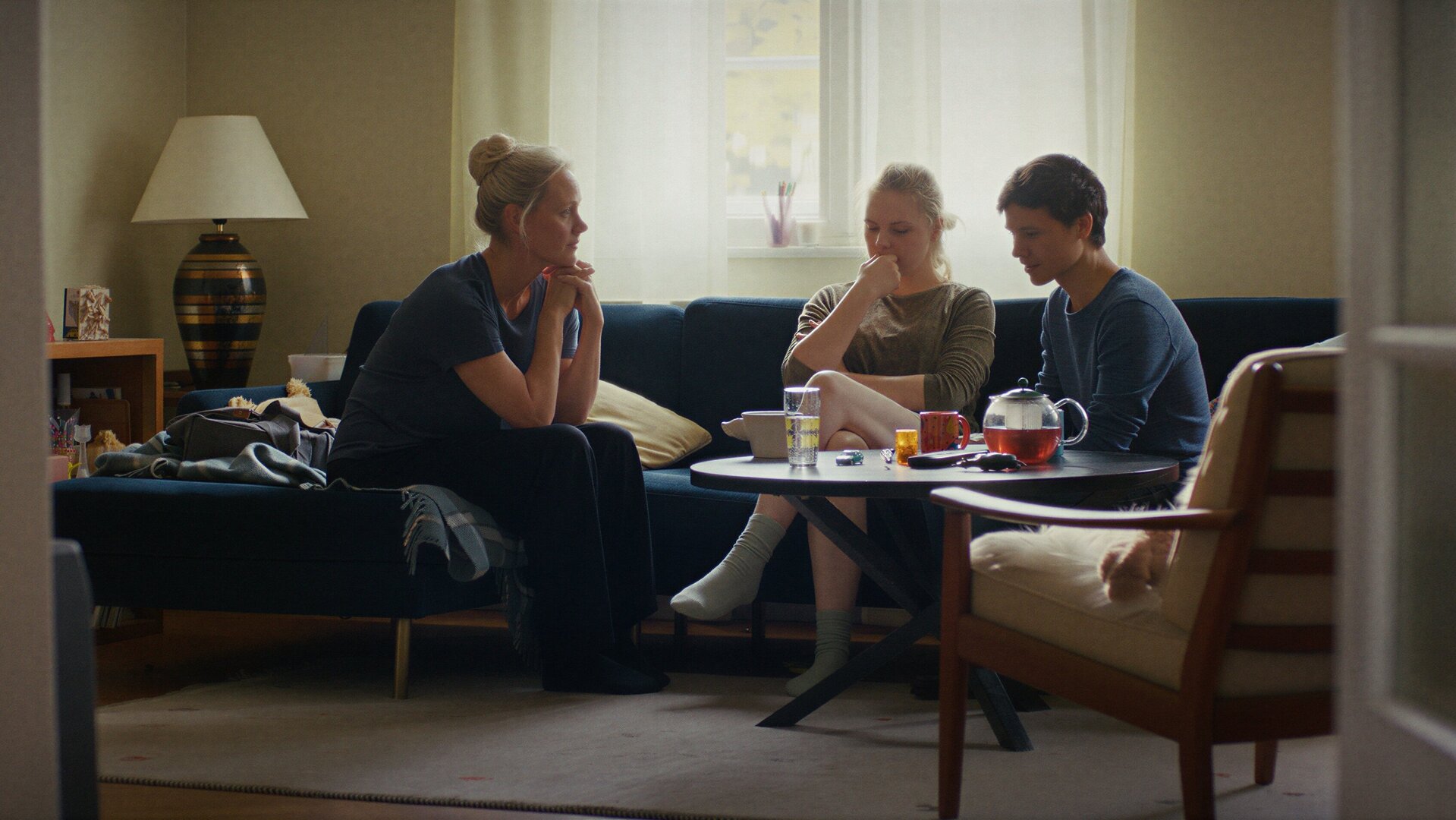"PUSH - Entscheidungen": Anna Koch (Anna Schudt) sitzt neben Romy (Ricarda Seifried) und Leo (Sebastian Urzendowsky) auf deren Sofa im Wohnzimmer. Romy und Leo sehen verzweifelt aus.