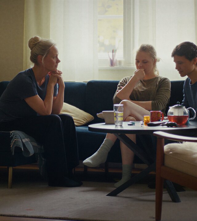 "PUSH - Entscheidungen": Anna Koch (Anna Schudt) sitzt neben Romy (Ricarda Seifried) und Leo (Sebastian Urzendowsky) auf deren Sofa im Wohnzimmer. Romy und Leo sehen verzweifelt aus.