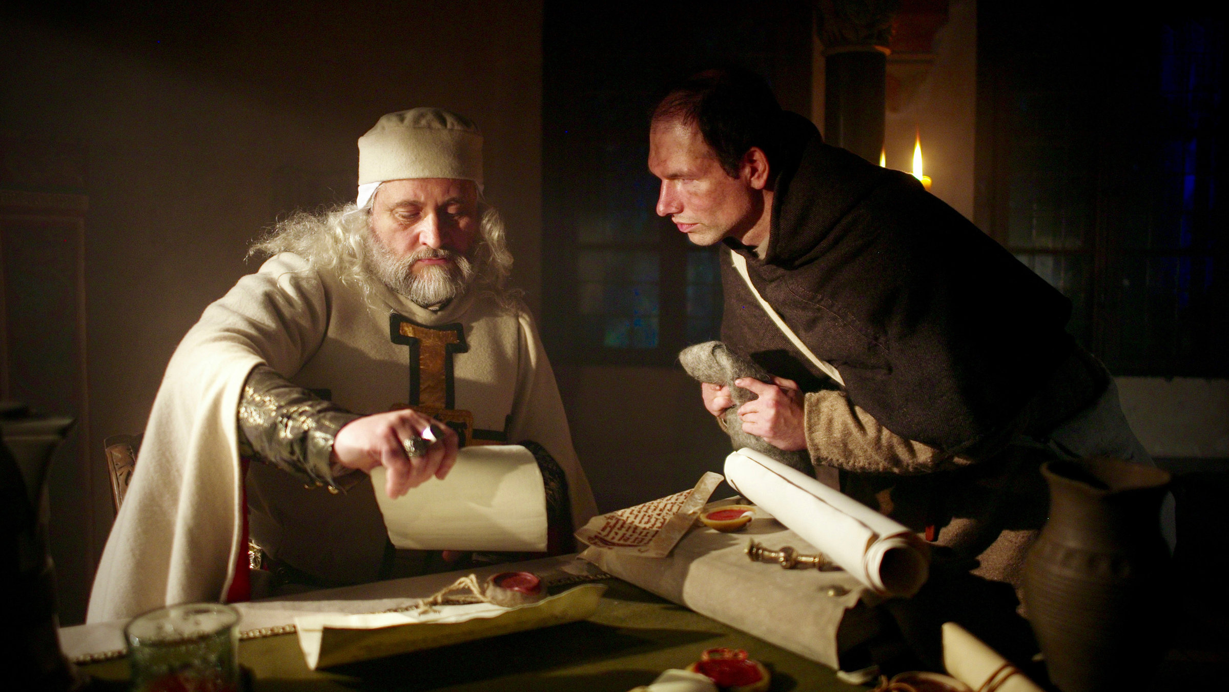 "Unter schwarzem Kreuz": Zwei Deutschritter betrachten an einem Tisch Dokumente (Spielszene).
