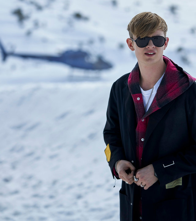 "Alex Rider - Point Blanc": Alex Rider (Otto Farrant) steht in einem Feld, dass schneebedeckt ist. Er trägt eine schwarze Sonnenbrille und blickt in die Ferne. Im Hintergrund steht ein Hubschrauber.