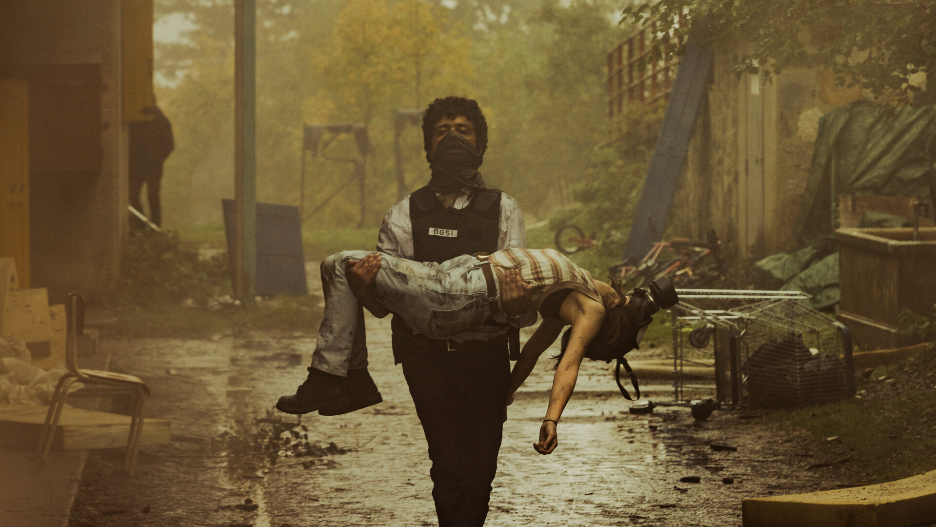 "Phoenix - Change Or Die: Wem gehört die Welt?": Polizist Amin Kacem (Mustapha Abourachid), ausgestattet mit einer schusssicheren Weste und mit einem Tuch vor dem Mund, trägt eine leblos wirkende Eloïse (Marie Colomb) in seinen Armen durch die rauchgeschwängerte Luft.