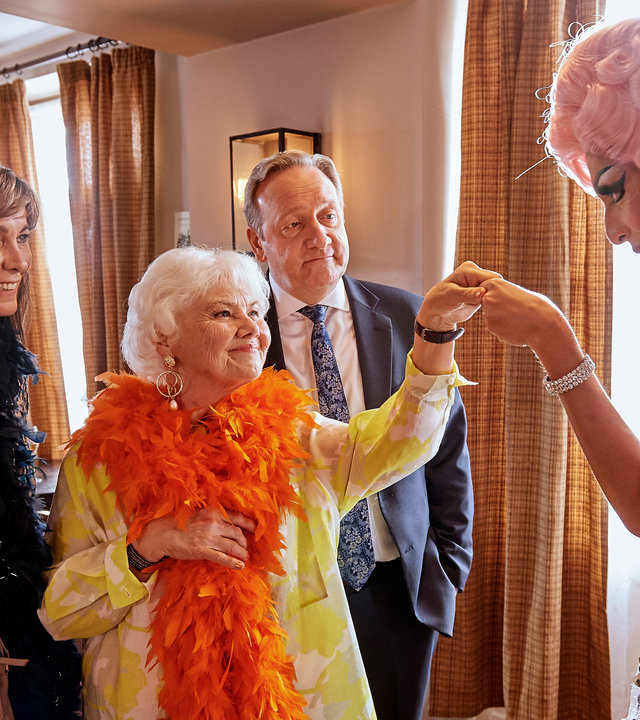 "Inspector Barnaby - Dressed To Kill": Sarah Barnaby (Fiona Dolman) und Rechtsmedizinerin Fleur Perkins (Annette Badland)  stehen mit John Barnaby (Neil Dudgeon) in einem Raum. Vor ihnen steht Malik Paynes (Felix Kai) als Dragqueen, bekleidet mit einem Paillettenkleid und einer langhaarigen, gelockten, Perücke.