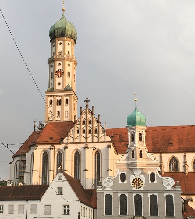 "Evangelischer Gottesdienst - Trotzdem gesegnet": Inmitten der Augsburger Altstadt befindet sich die Stadtpfarrkirche St. Ulrich und Afra. Ihr hoher Zwiebelturm und das langgestreckte Kirchengebäude überragen die umliegenden Häuser. Das spätgotische Ensemble mit der evangelischen Kirche St. Ulrich ist ein beeindruckendes Fotomotiv, das auch die Augsburger Parität symbolisiert.