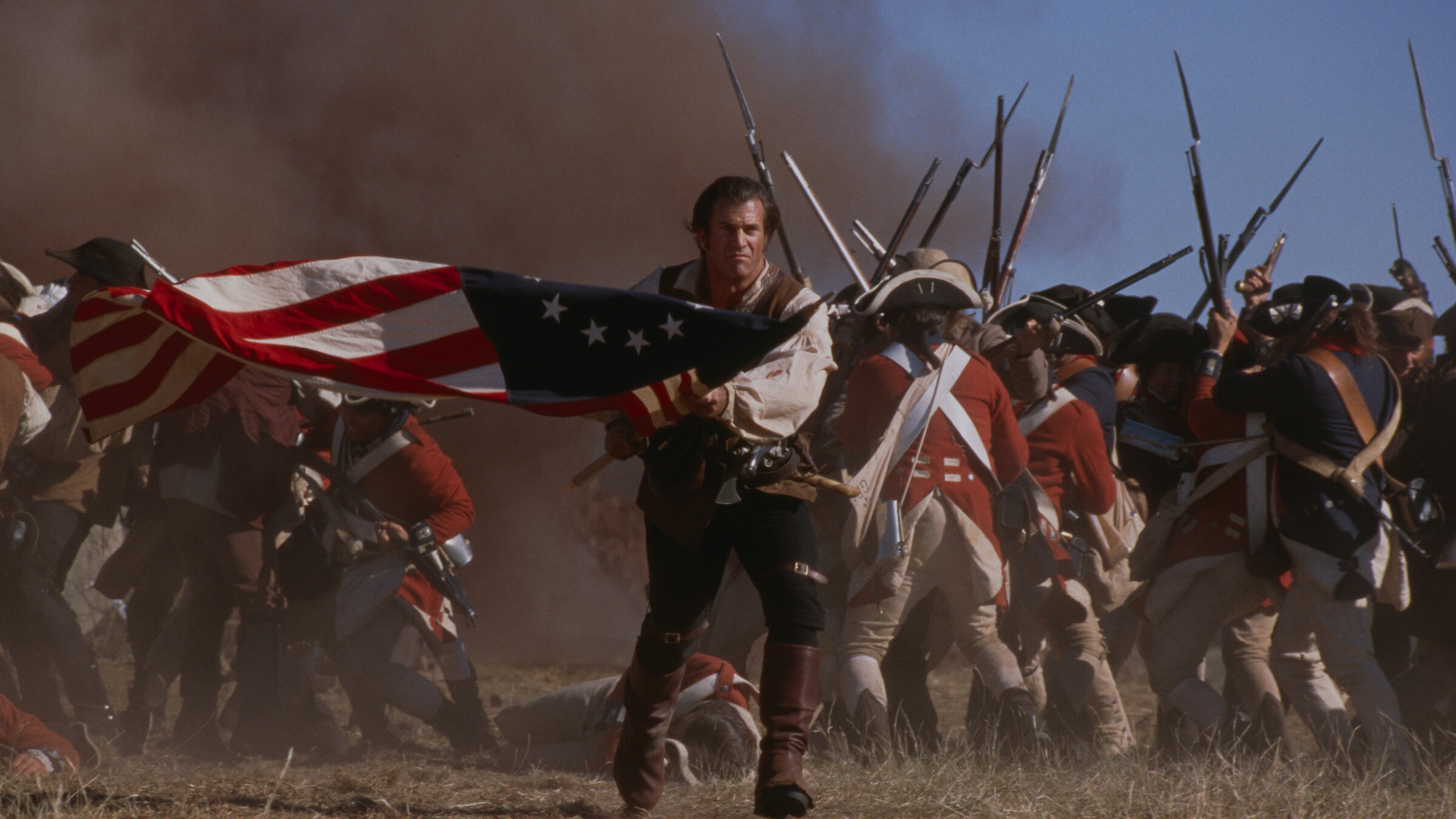 „Der Patriot“: Benjamin Martin (Mel Gibson) stürmt mit einer US-Flagge in den Händen in den Kampf. Hinter ihm sieht man Soldaten in roter Uniform.