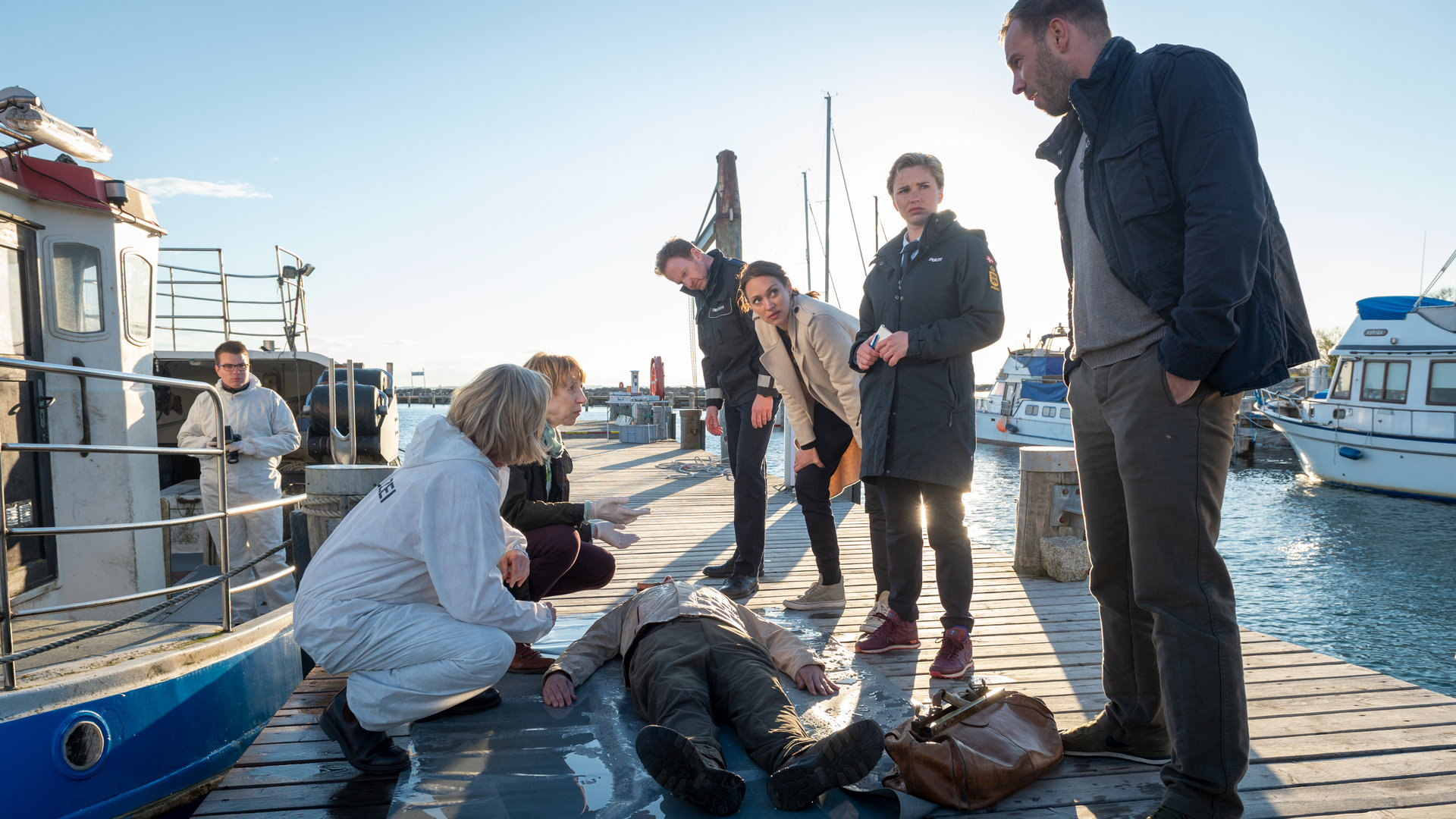 "SOKO Wismar – Die Schildkröte": Auf einem Bootsanleger am Hafen stehen die Kommissare Joost (Nike Fuhrmann) und Pöhlmann (Dominic Boeer) sowie die Polizisten Stine (Sidsel Hindhede) und Timmermann (Mathias Junge) neben dem Leichnam von Willi Seeberg (Peter Rauh). Links vom Toten knien Roswitha Prinzler (Silke Matthias) und Helene Sturbeck (Katharina Blaschke).