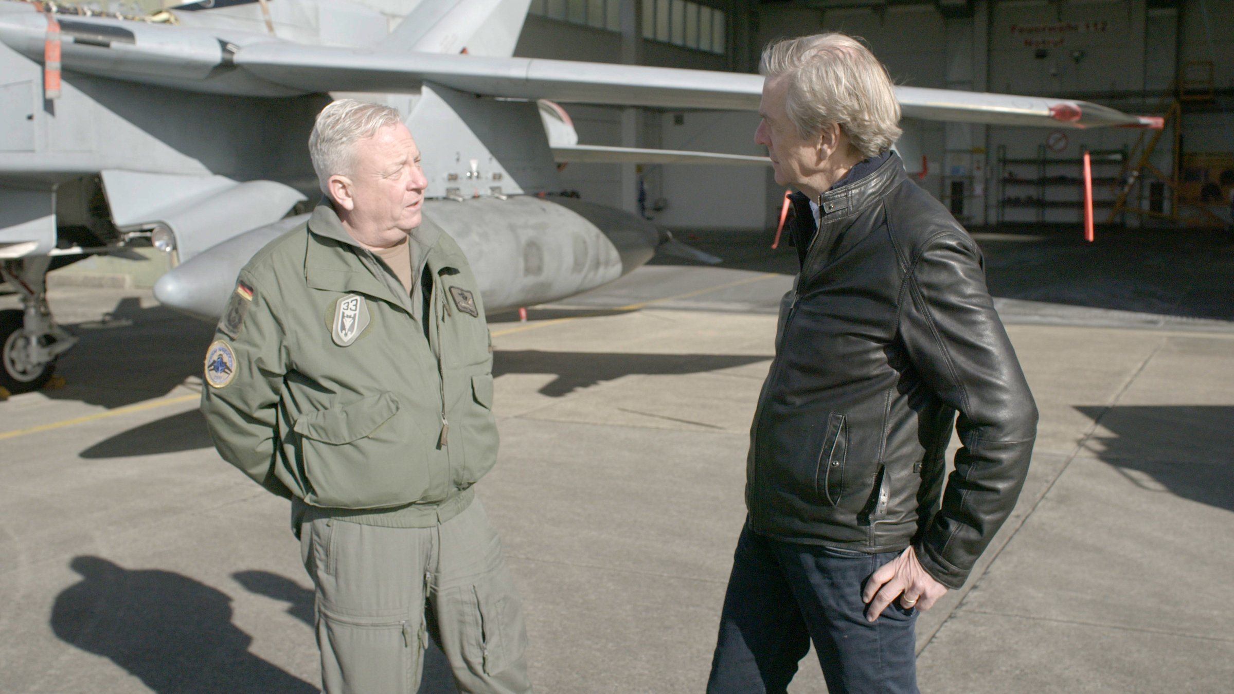 "ZDFzeit: Putins Tabubruch - die neue Angst vor der Bombe": Oberst Thomas Schneider und Claus Kleber stehen vor einem Kampfflugzeug und unterhalten sich.