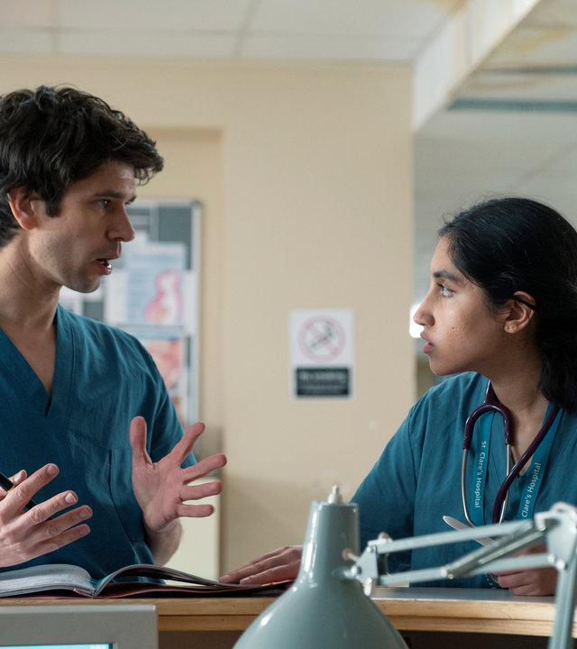 "This Is Going To Hurt - Sisyphos ist müde": Shruti (Ambika Mod) und Adam (Ben Whishaw) lehnen an der Rezeption einer Krankenstation und unterhalten sich.