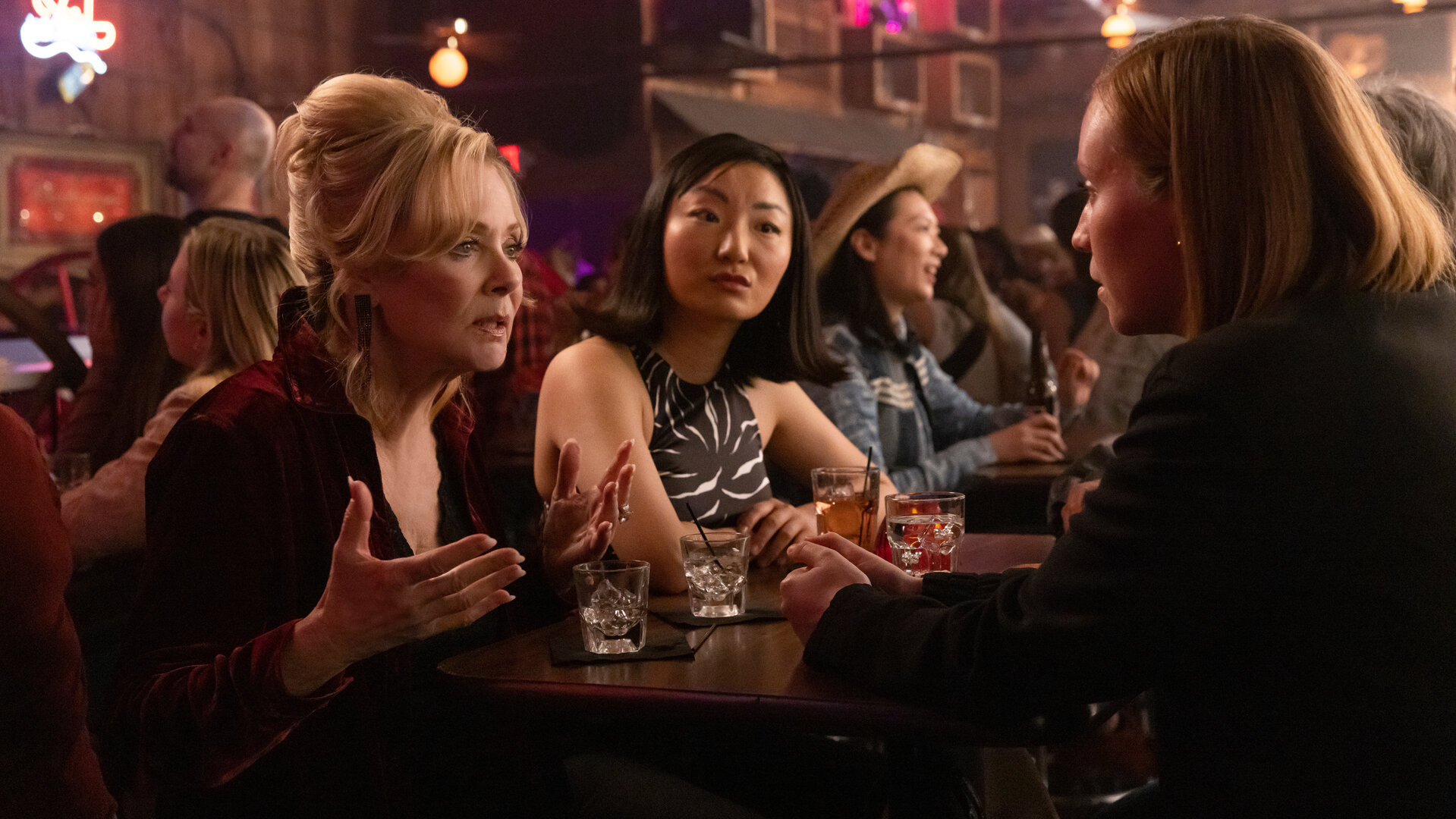 "Hacks - Mädelsabend, jung und alt": In einer belebten Bar: Deborah (Jean Smart) spricht ernst gestikulierend zu Ava (Hannah Einbinder), während Kiki (Poppy Liu) mit neutralem Gesichtsausdruck zu Ava schaut.