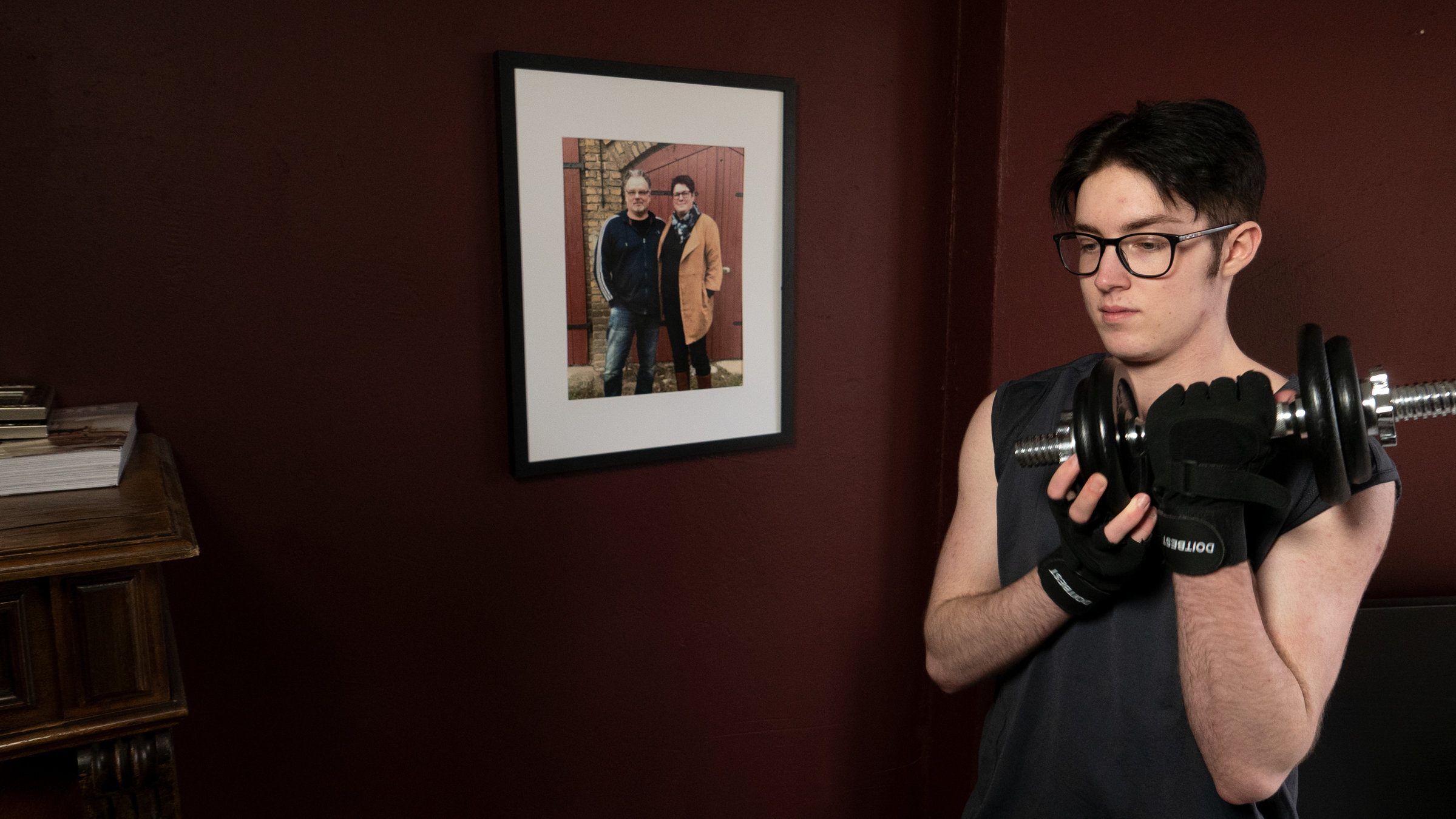 "37°: Glücklich erst als Junge - Wenn aus der Tochter ein Sohn wird": René steht mit einer Hantel in der Hand im Zimmer vor einem Foto seiner Eltern.