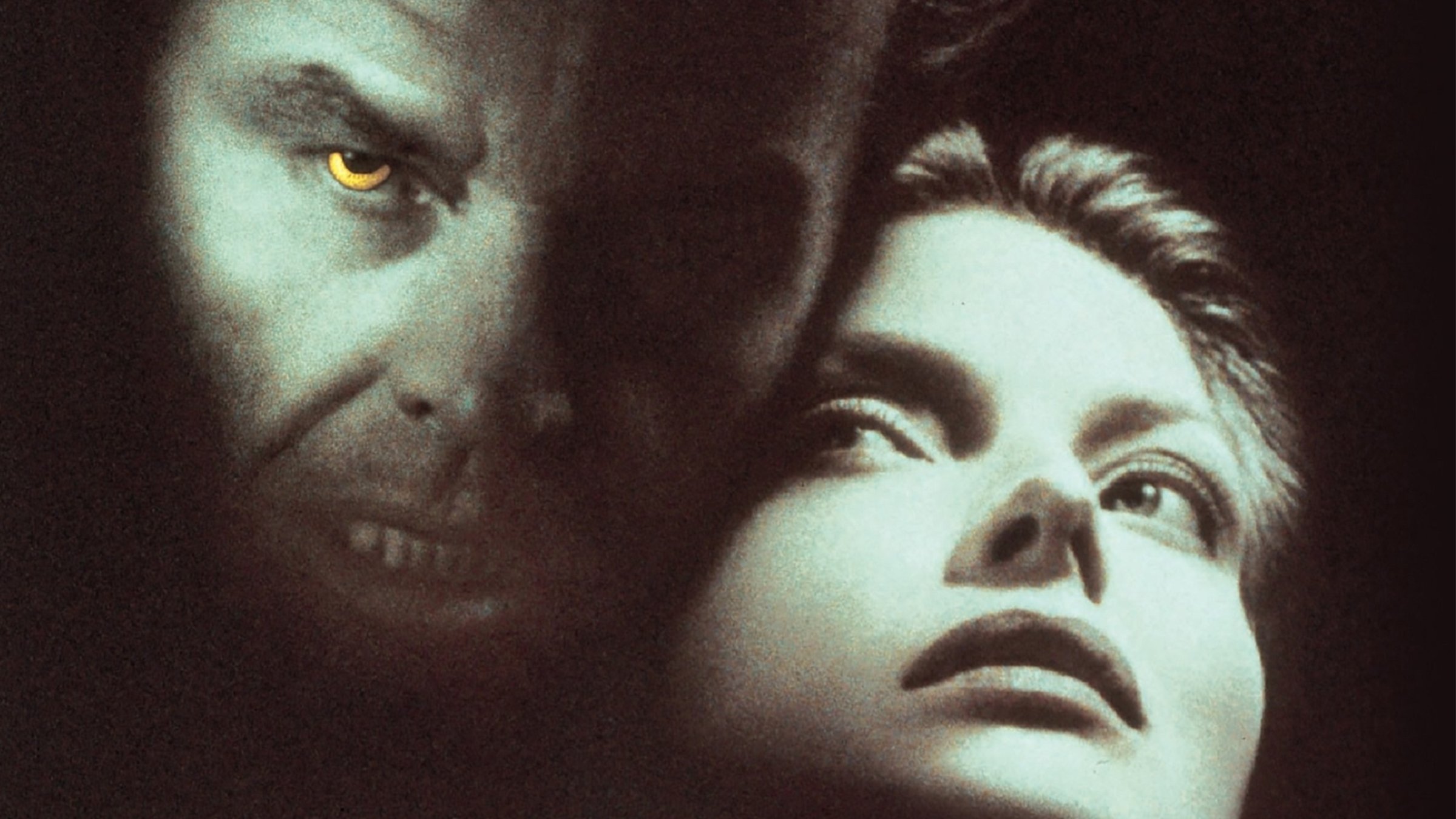 "Wolf – Das Tier im Manne": Will Randall (Jack Nicholson) ist gesichtsgroß zu sehen, mit leicht geöffnetem Mund und Zähnen, vor allem aber mit gelb leuchtenden Augen. Rechts neben ihm zu sehen ist das Gesicht Lauras (Michelle Pfeiffer), die forschend-neugierig zu ihm blickt. Beide Gesichter sind vor dunklem Hintergrund schlaglichtartig erhellt.