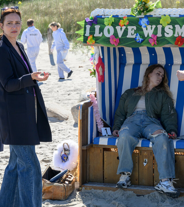 „SOKO Wismar – Tod im Strandkorb“: Kriminalhauptkommissar Lars Pöhlmann (Dominic Boeer), Kriminalhauptkommissarin Karoline Joost (Nike Fuhrmann) und Rechtsmedizinerin Dr. Helene Sturbeck (Katharina Blaschke) haben sich an einem Strandkorb um die Leiche der Influencerin Carina Wilde (Kleindarstellerin) versammelt.