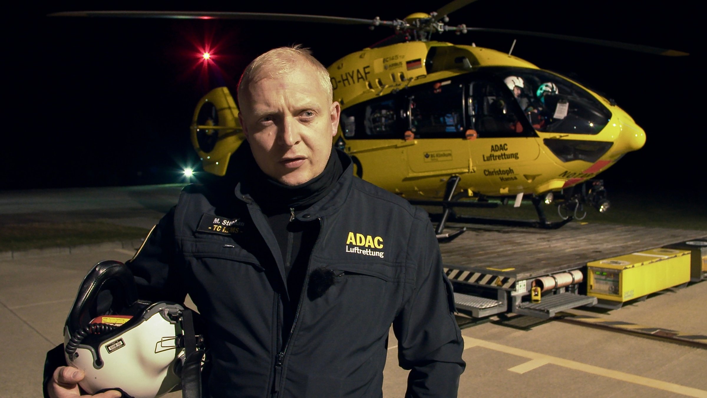 "37° Guten Morgen Feierabend! - Leben mit der Nachtschicht": Der Notfallsanitäter Martin steht vor dem gelben ADAC-Hubschrauber, er hält seinen Helm im Arm.