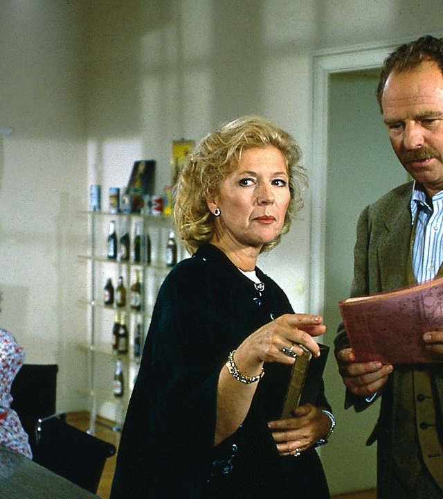 "Das Erbe der Guldenburgs - Der unfreiwillige Vater": Christine (Christiane Hörbiger) berät mit Hannes von Mehringen (Friedrich von Thun). Von Mehringen hält einen roter Ordner, Im Hintergrund beobachtet Frau Reinders (Astrid Mayer-Gossler) das Geschehen.