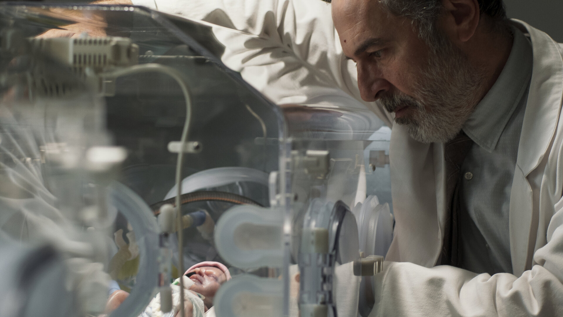 "Doktor Ballouz - Nur ein Wunder": Nahaufnahme: Dr. Ballouz (Merab Ninidze) blickt sorgenvoll auf ein neugeborenes Baby in einem Inkubator.