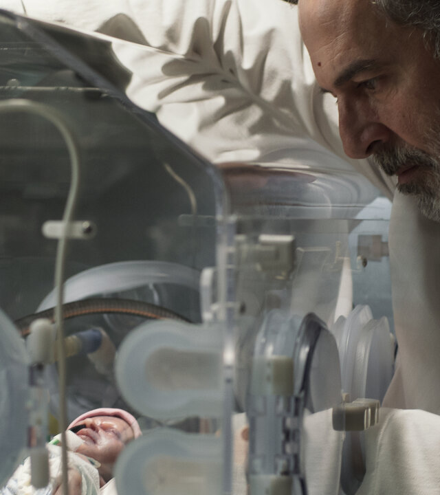 "Doktor Ballouz - Nur ein Wunder": Nahaufnahme: Dr. Ballouz (Merab Ninidze) blickt sorgenvoll auf ein neugeborenes Baby in einem Inkubator.