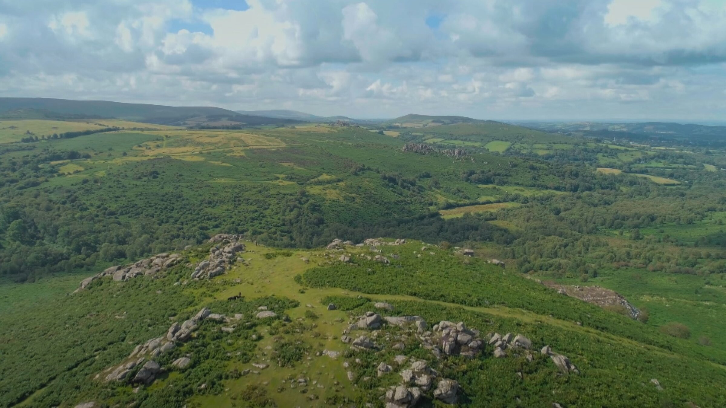 „Großbritanniens schönste Bahnstrecken - Die Dartmoor-Linie“: Eine hügelige Landschaft, die mit Wiesen, Büschen und Felsen bedeckt ist.