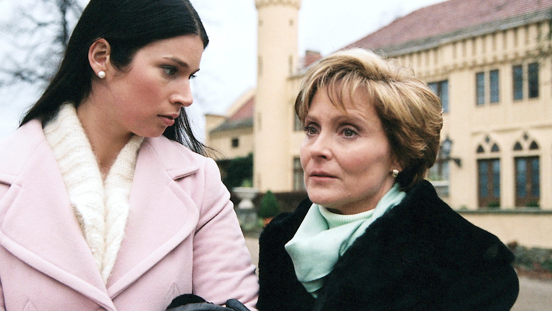 "Bianca - Wege zum Glück: Kapitel 98": Spaziergang vor dem Gutshof: Judith (Elisabeth Sutterlüty) dreht sich hin zu Ariane. Ariane (Kerstin Gähte) hat sich bei Judith im Arm eingehängt und schaut gedankenverloren vor sich hin.