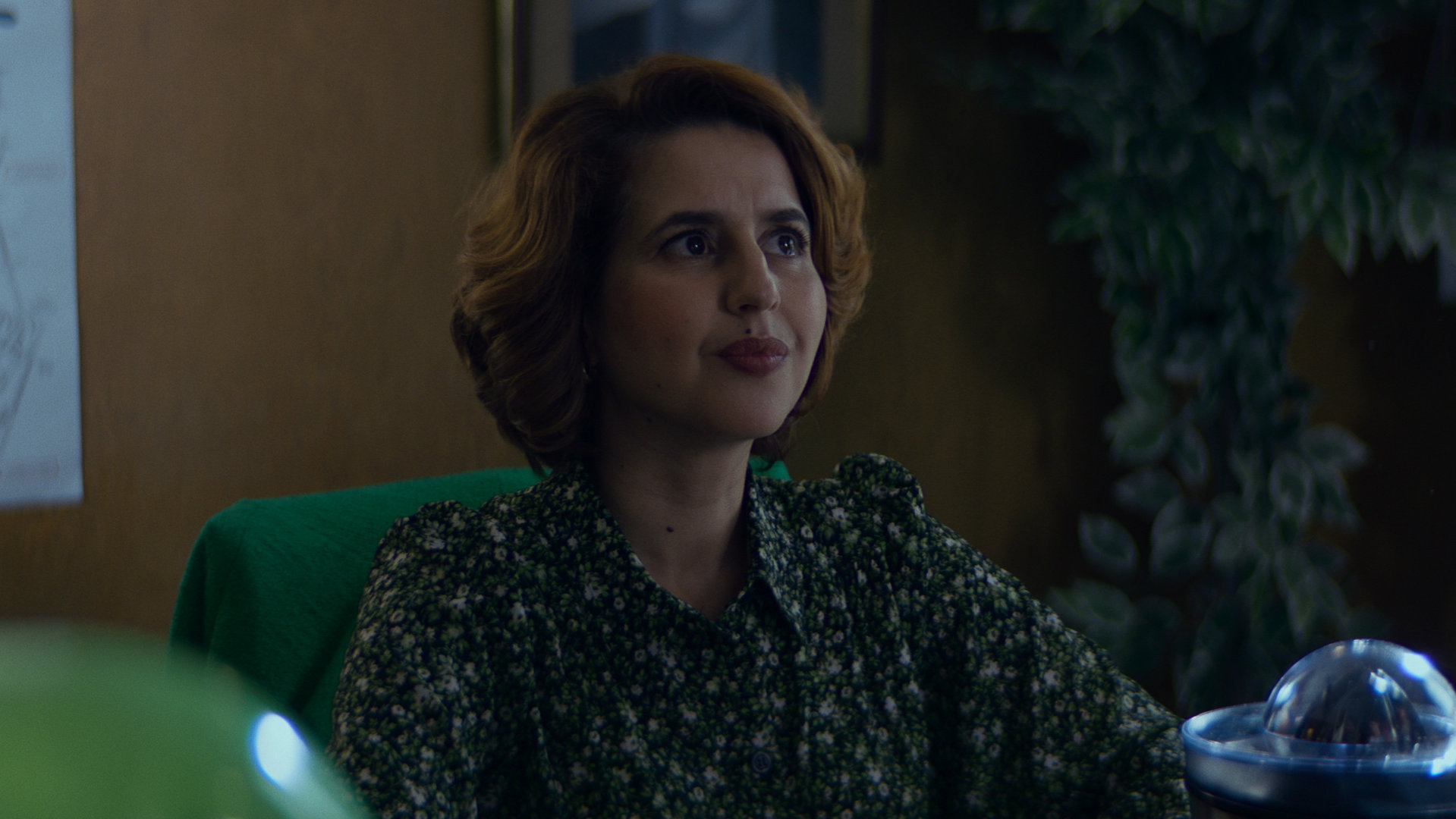 "Derby Girl - Schluss mit Rollschuhen": Yasmine Jouvion (Nadia Roz) sitzt an einem Schreibtisch und schaut aufmerksam nach vorne.