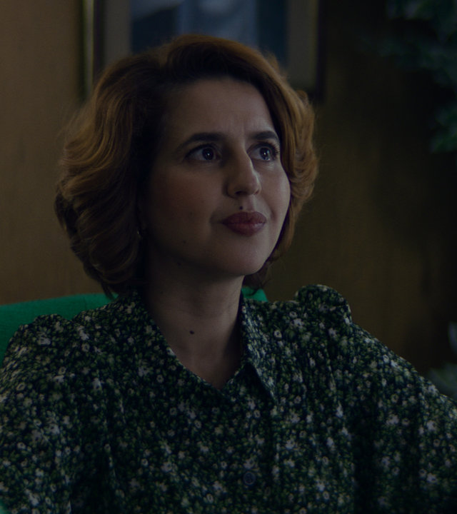 "Derby Girl - Schluss mit Rollschuhen": Yasmine Jouvion (Nadia Roz) sitzt an einem Schreibtisch und schaut aufmerksam nach vorne.