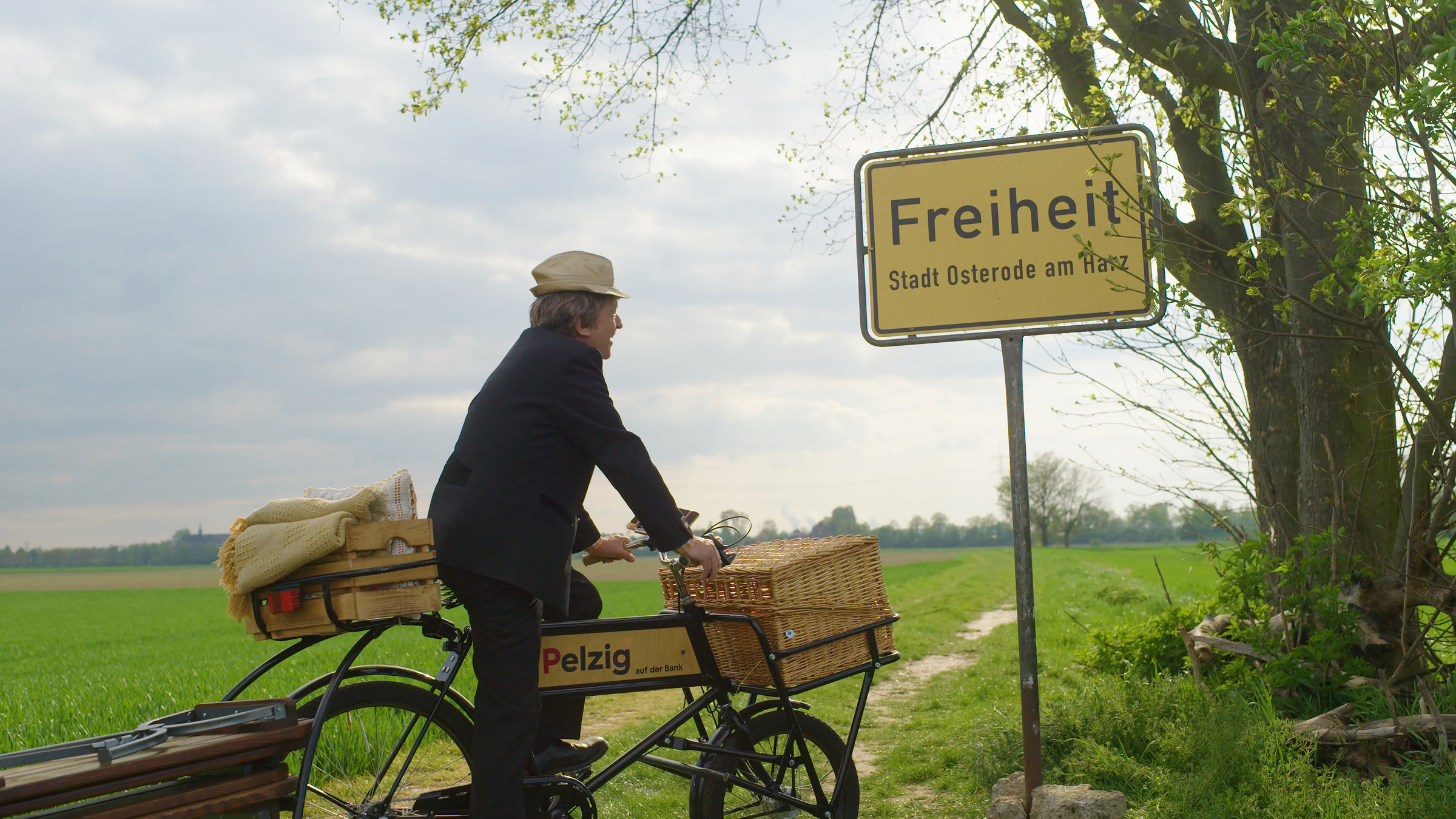 "Beim Pelzig auf der Bank - Scheiß Freiheit": Pelzig steht mit seinem Fahrrad vor einem Ortsschild mit der Aufschrift Freiheit.