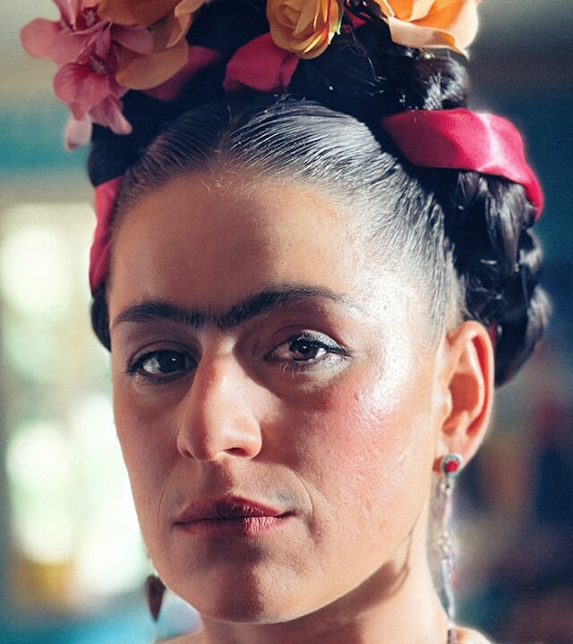 "Sketch History - Gute Fridas, schlechte Fridas": Frida Kahlo (Lou Strenger) steht in einem sehr bunten Raum. Sie ist stark geschminkt und ihre Augenbrauen gehen ineinander über. Sie trägt eine bunte mexikanische Tracht mit einem üppigen Blumenkranz in den Haaren.