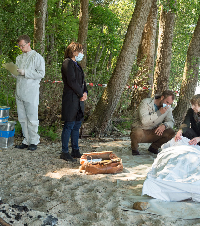 "SOKO Wismar – Todesstrafe": An einer Strandbucht zwischen Bäumen ist ein Tatort abgesperrt. Helene Sturbeck (Katharina Blaschke) kniet auf dem Boden hebt leicht das Leichentuch an. Neben ihr kniet Lars Pöhlmann (Dominic Boeer), der sich einen Mundschutz vor das Gesicht hält. Etwas abseits steht Katrin Börensen (Claudia Schmutzler), ebenfalls mit Mundschutz. Außerdem sind die Kollegen von der KTU (Komparsen) bereits bei der Arbeit.