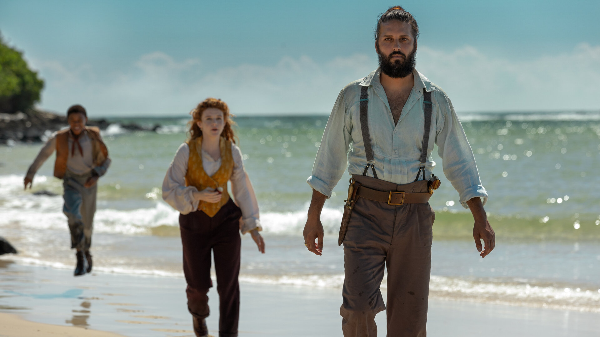 "Nautilus - Die unbekannte Insel": Nemo (Shazad Latif), Humility (Georgia Flood) und Blaster (Kayden Price) laufen hintereinander über einen Strand. Im Hintergrund liegt das Meer.