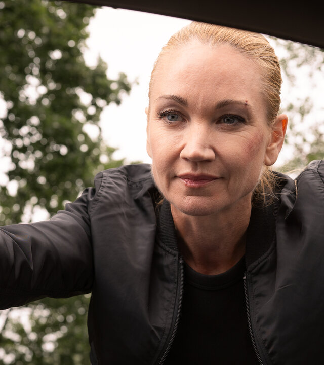 "Sarah Kohr – Bis auf den Grund": Sarah Kohr (Lisa Maria Potthoff) schaut selbstsicher lächelnd durch das Fenster in das Innere eines Wagens.