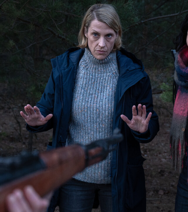 "SOKO Potsdam - Nachts im Wald": Im dichten Wald stehen Tamara Meurer  (Anja Pahl) und Pauline Hobrecht (Agnes Decker), die ihre Hände abwehrend hochhalten. Tamara Meurer blickt ernst und konzentriert nach vorn, neben ihr steht Pauline Hobrecht. Vor beiden ist ein Gewehrlauf auf sie gerichtet.