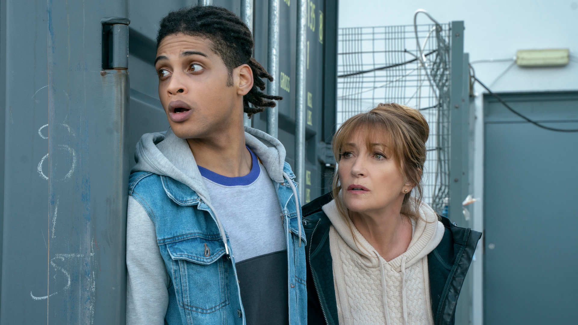 "Harry Wild - Mörderjagd in Dublin: Operation Mincemeat": Harry Wild (Jane Seymour) und Fergus Reid (Rohan Nedd) verstecken sich hinter einem grauen Container.