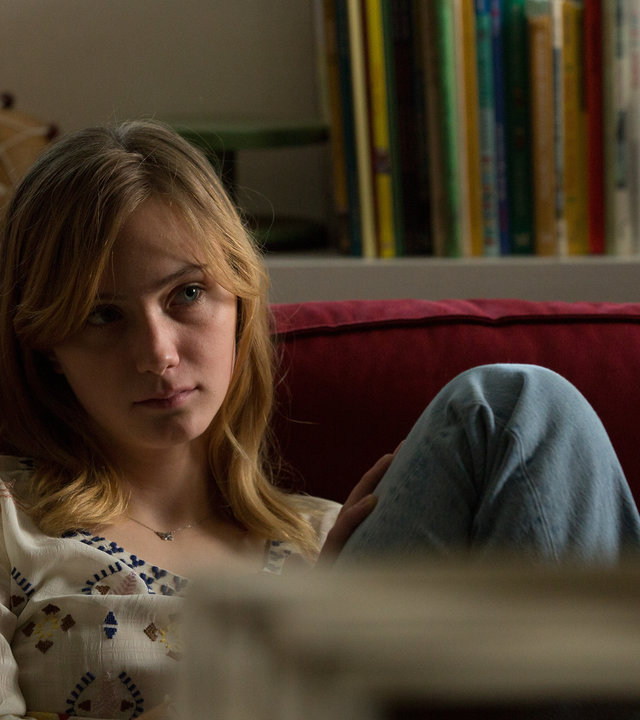 "SAFE - Episode 8": Nellie (Carla Hüttermann) sitzt auf einem Sofa und sieht in die Ferne. Im Hintergrund sind Bücher und diverse Dekorationsgegenstände zu sehen.