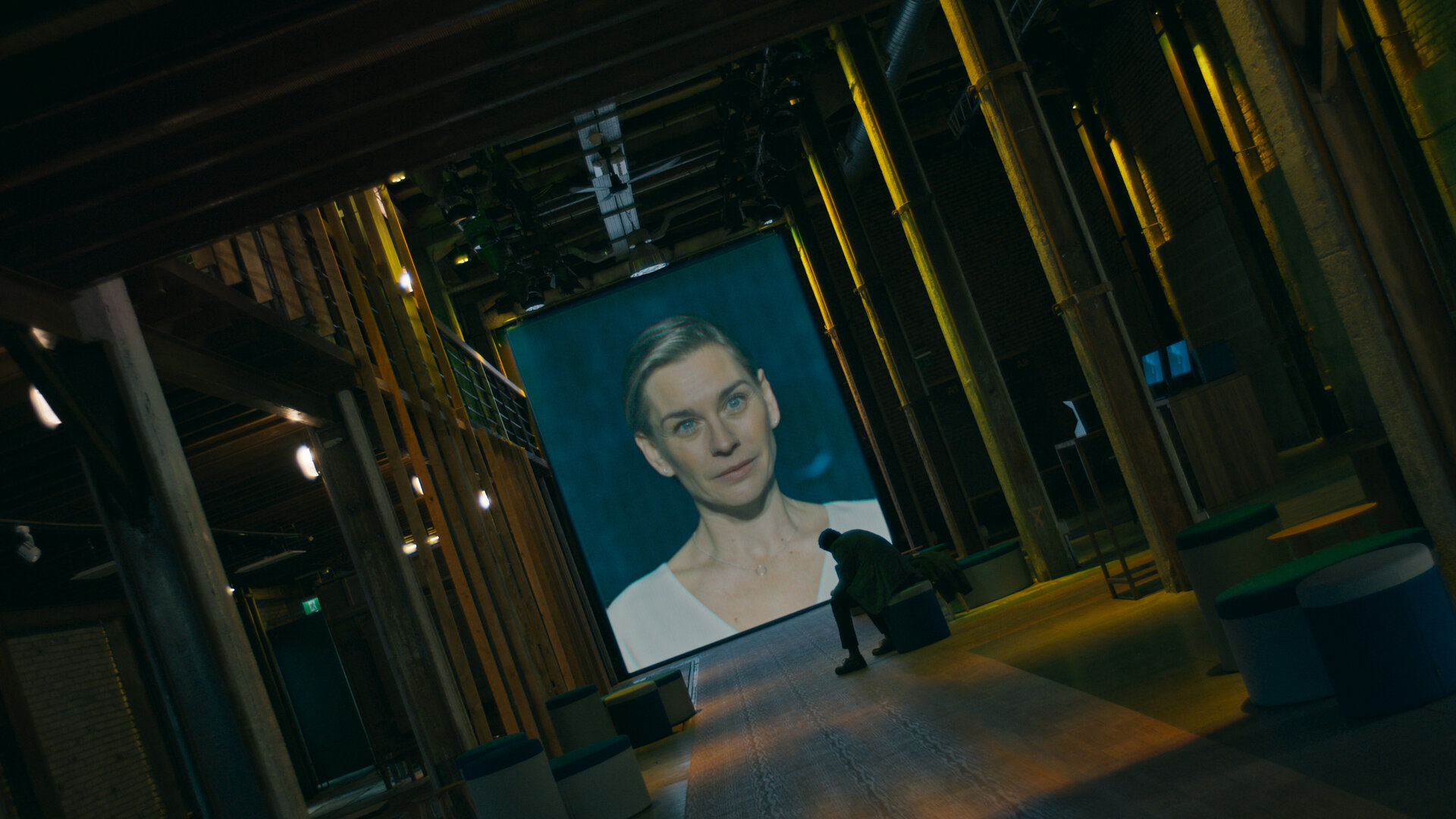 "Concordia - Tödliche Utopie (6) - Kein Weg zurück": Juliane Ericksen (Christiane Paul) ist auf eine Leinwand projiziert. Davor sitzt Noah Ericksen (Steven Sowah) in einem dunklen Raum und sieht zu.