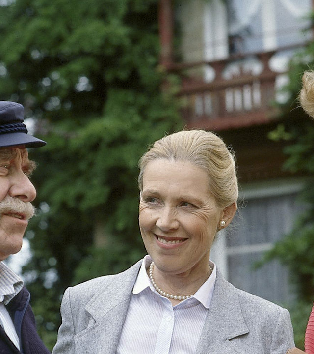 "Zwei Münchner in Hamburg - Von Frau zu Frau": Julia (Uschi Glas) die Leiterin des Seemannshauses (Kyra Mladek) und Kapitän Kodass (Ferdinand Dux) stehen gemeinsam vor einem Haus und lächeln sich gegenseitig an.